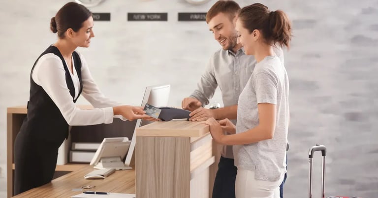 A couple checks into a hotel at the reception desk using a credit card for payment with a smiling receptionist.