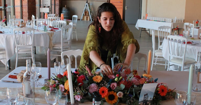 Estelle, créatrice de l’Ensorce’Fleurs, décore une table de mariage avec un bouquet coloré.