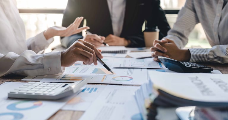 picture of hands of 3 people worgin on documents a table 