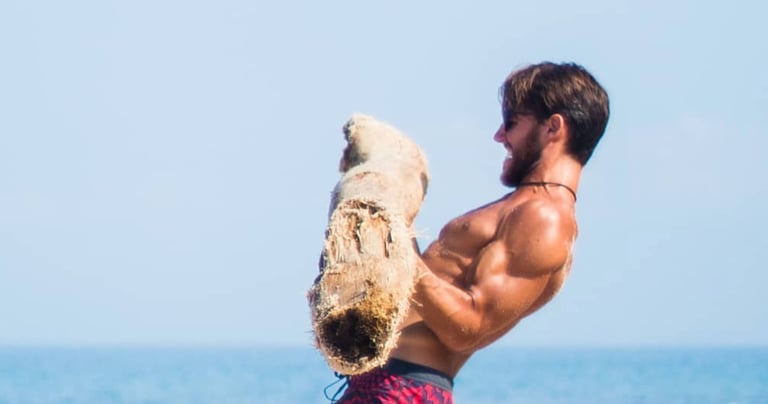 a strong man lifting a log on a beach 