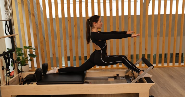 Uma mulher a realizar um alongamento em abertura no reformer num estúdio moderno 