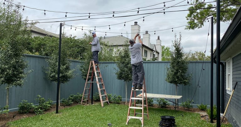 landscape lighting technicians installing patio string lights with poles