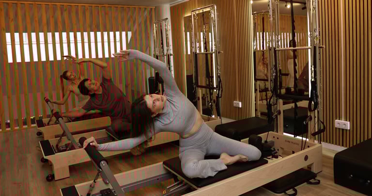 Three people performing a side stretch on reformers in a Pilates studio with wooden accents 