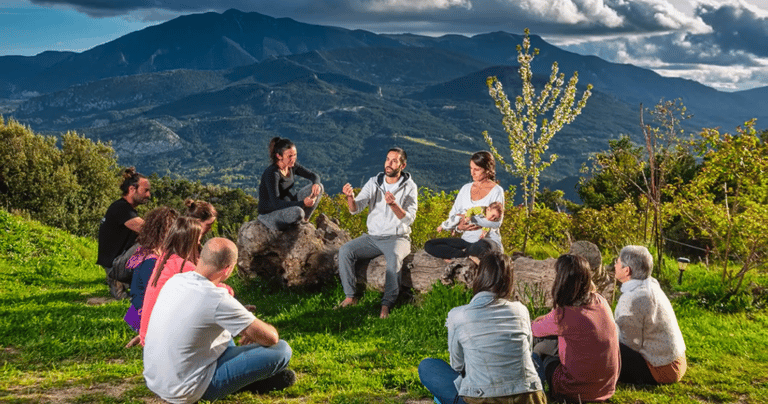 A group of people sitting in a circle on a grassy mountain hill for an outdoor wellness retreat.