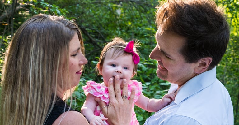A happy couple holding the child and gazing at her. The child glances at the camera, smiling slightly. 