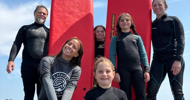 A happy family in wetsuits posing with red longboard surfboards on a sunny beach during a surf lesson.