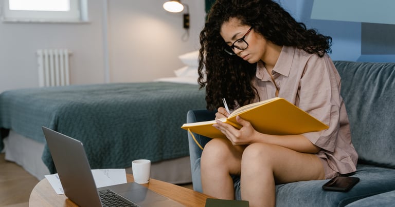 a woman sitting on a couch with a laptop and a notebook