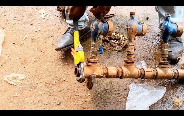 Plombier réparant un compteur d'eau principal et des tubes rouillés à la clé.