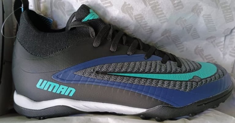 Zapatos de fútbol para césped artificial Uman en negro y azul con detalles en turquesa.