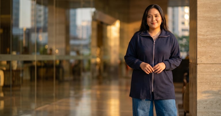 Smiling young woman in a navy blue zip-up cardigan and jeans standing in a modern building lobby.