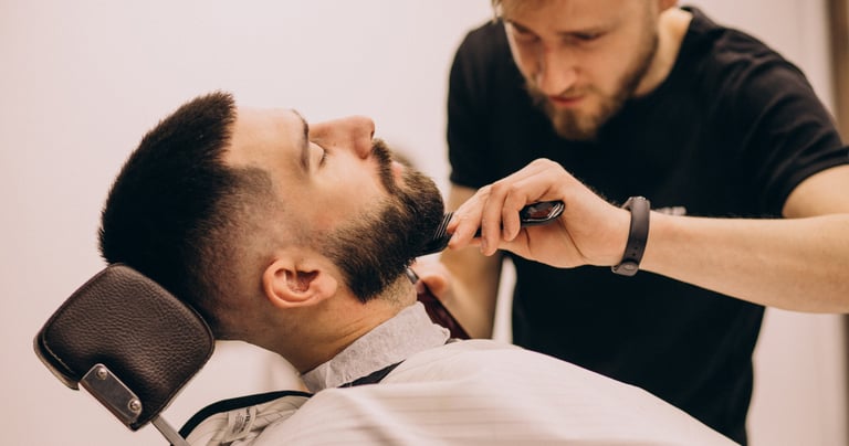 Professional barber grooming a client's beard with a comb at a modern barbershop.
