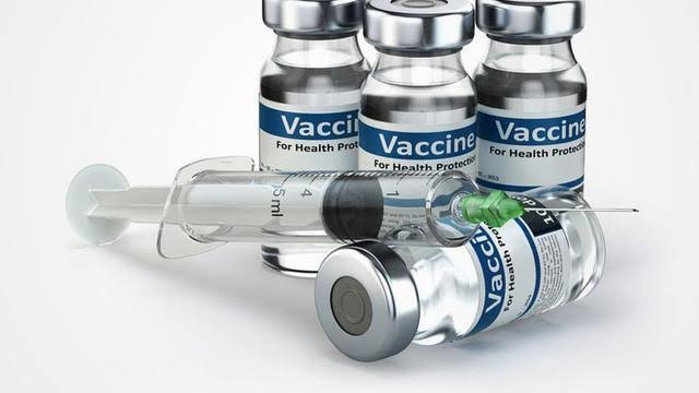 Medical glass vaccine vials with blue labels and a sterile hypodermic syringe for immunization injections.