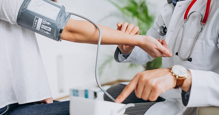 A doctor in a white coat takes a patient's blood pressure using a digital monitor and cuff.