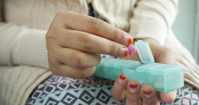 A person taking a pink pill from a green daily medication organizer for health management.