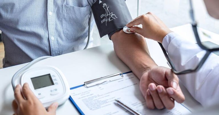 A doctor checking a patient's blood pressure using a digital monitor and stethoscope at a medical clinic.