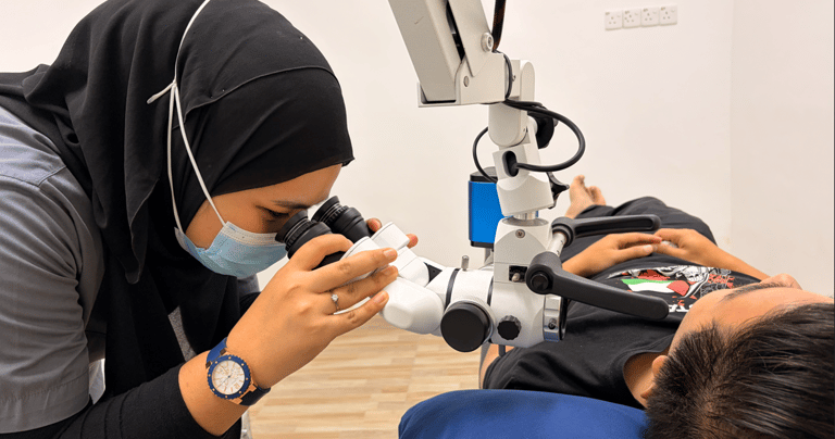 A female dentist in a hijab using a dental microscope to examine a patient during a procedure.