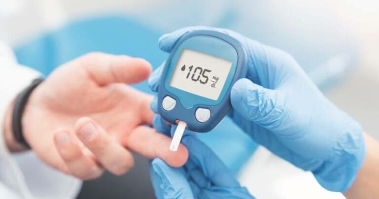 A healthcare professional in blue gloves uses a digital glucose meter to test a patient's blood sugar levels.