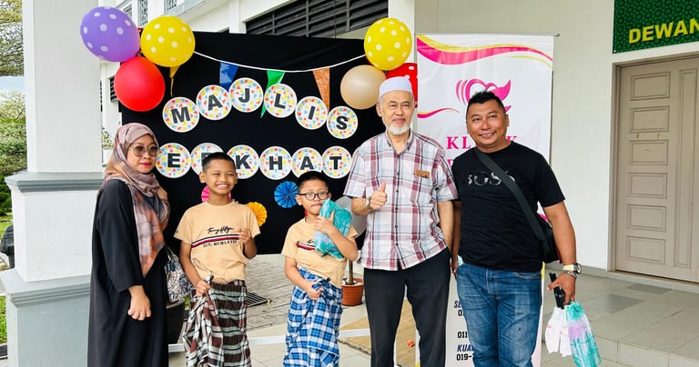 A family posing at a Majlis Berkhatan circumcision ceremony event with colorful balloons and banners.