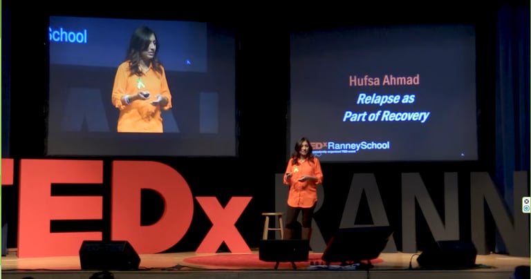 A woman in an orange shirt speaks energetically on stage. The screen reads "Hufsa Ahmad: Relapse as Part of Recovery."