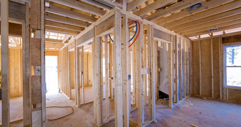 Interior view of a home under construction showing wood stud framing, exposed plumbing, and electrical rough-in