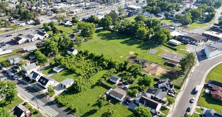 Aerial drone view of a vacant infill lot surrounded by a residential neighborhood and nearby park.