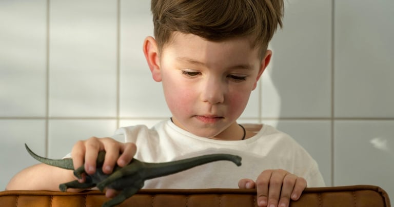 a young boy sitting in a suitcase with a dinosaur toy