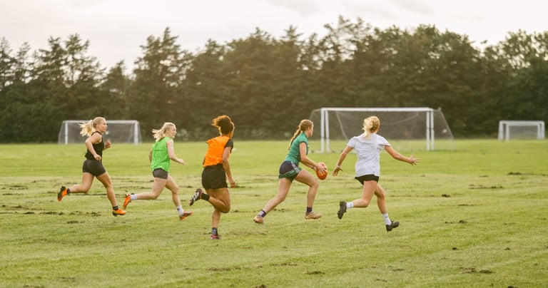 A group of women from the West London Wildcats run across a field kicking an AFL Football.