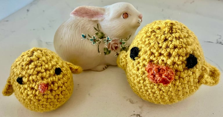 2 small yellow crocheted chicks with a ceramic Easter bunny behind them.