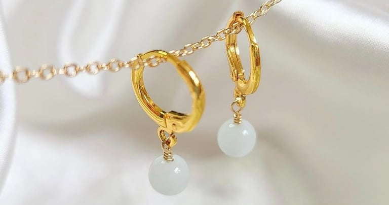 Aros de oro con gotas de piedras preciosas blancas que cuelgan de una cadena de oro sobre tela.