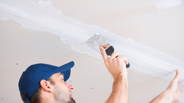 a man in a blue hat and a blue hat is texture matching and finishing a ceiling