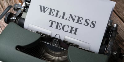A typewriter with a sheet of paper in the carriage displaying the text 'WELLNESS TECH'. The typewrit