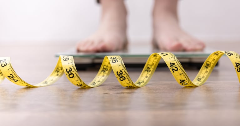 Sustainable fat-loss coaching—person stepping on scales with tape measure, weekly check-ins 