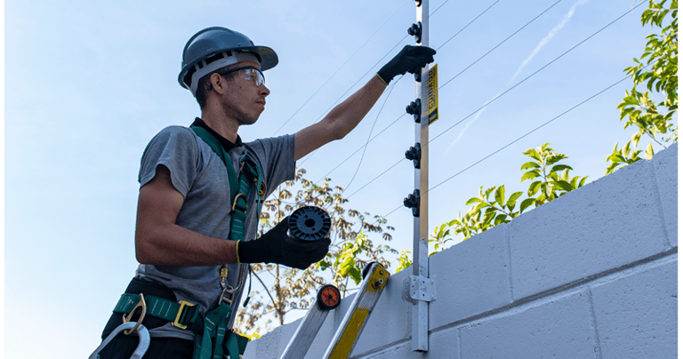 Professional technician installing an electric security fence on a white perimeter wall.