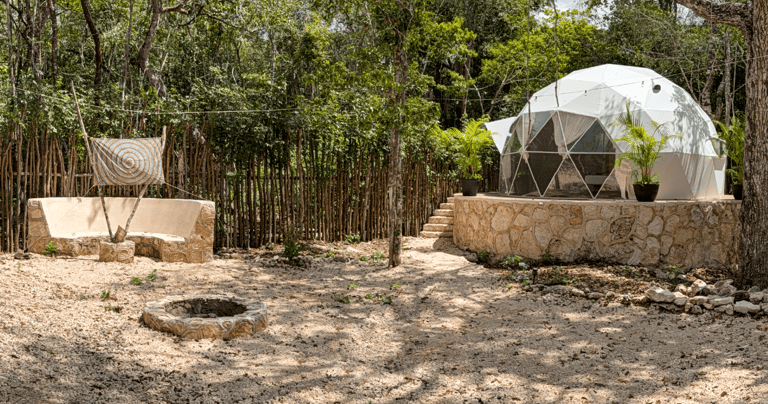 Luxury geodesic dome for glamping with fire pit and outdoor seating in a lush Mayan rainforest setti