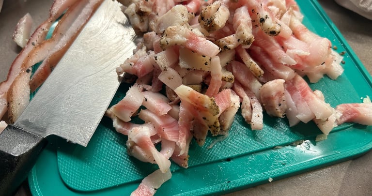 Slices of raw guanciale cured pork jowl with black pepper on a green cutting board.