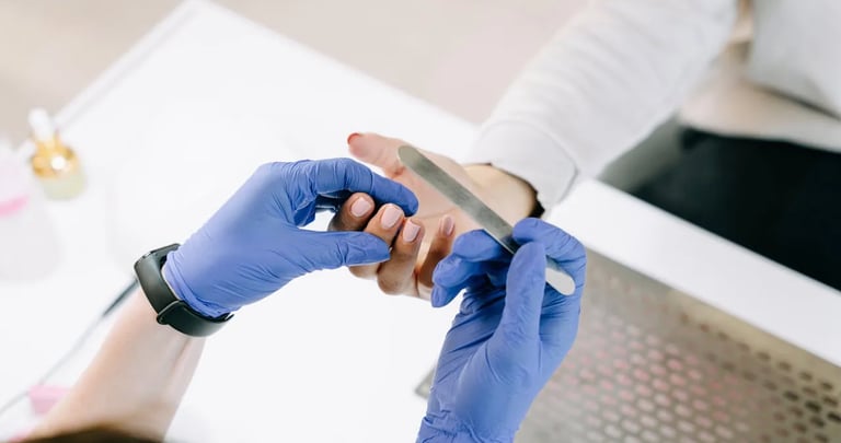 A manicurist with gloves fixing a customer's nail.