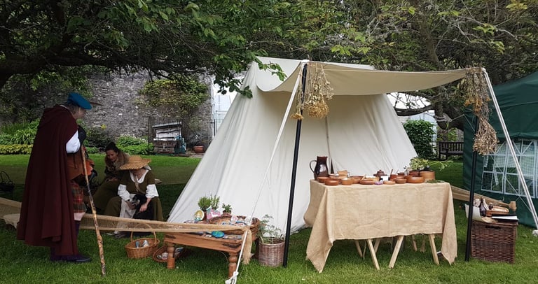 reenactors talking beside a medieval tent with a table of herbal remedies