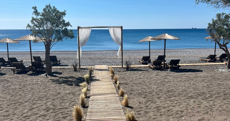 Wooden walkway leading to a beachfront wedding arch with sunbeds and umbrellas on a sandy beach.