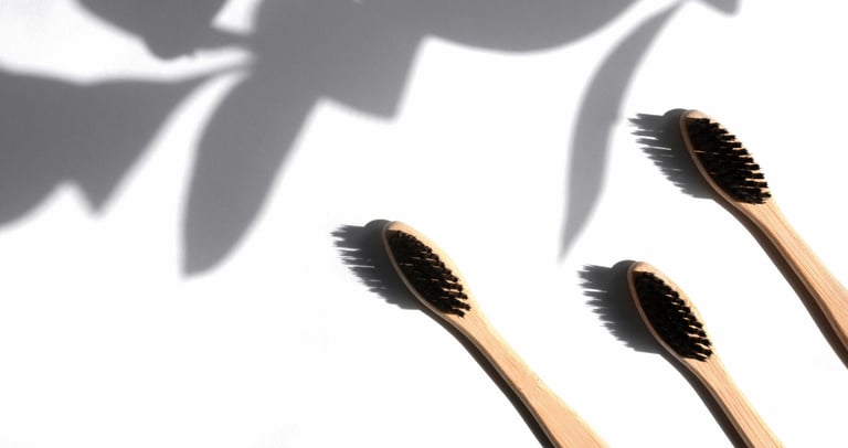 three wooden toothbrushes with a shadow of a plant