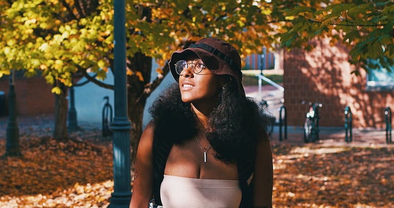 Young college black woman smiling and birdwatching underneath golden yellow autumn trees.
