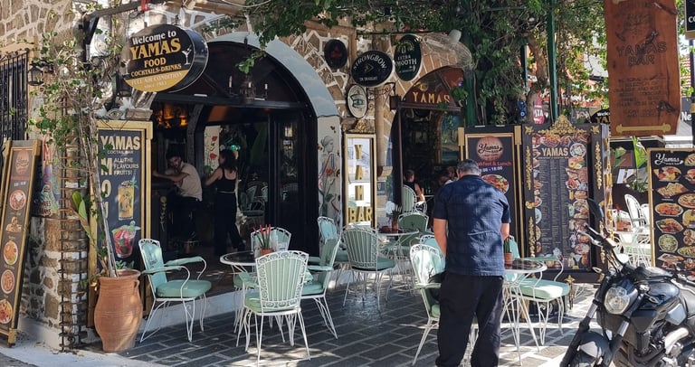 Charming outdoor seating area at Yamas bar and restaurant with Greek stone architecture and palm trees.