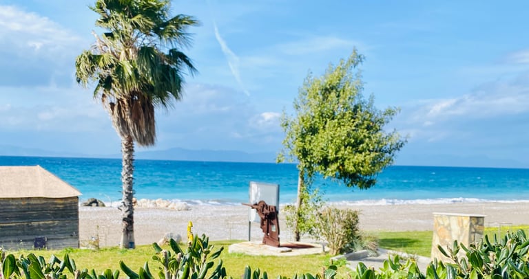 Tropical beach landscape with green shrubs, palm trees, and a historic cannon overlooking the blue sea.