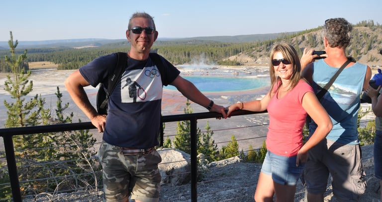 a man and woman standing on a railing railing overlooking the grand prismatic spring in yellowstone