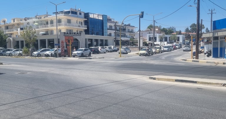 A sunny street intersection in Faliraki, featuring cars parked near shops and a clear blue sky.