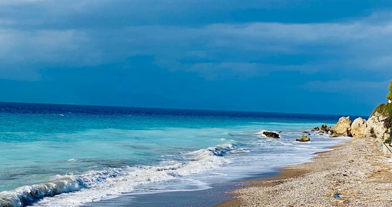 Pebble beach with turquoise ocean waves under a dramatic cloudy blue sky.