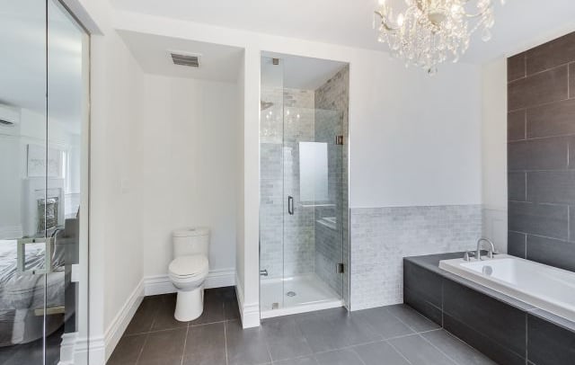 a large master bathroom with a toilet, shower stall, and soaker tub tiled in black