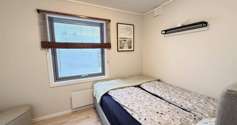 Modern guest bedroom with a twin bed, patterned bedding, neutral walls, and a window with wooden blinds.