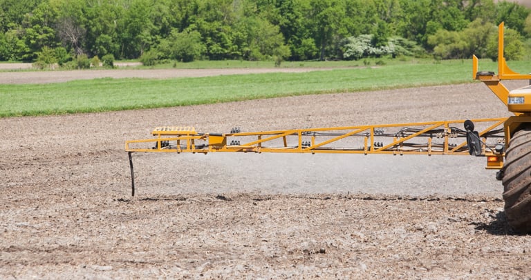 Agricultural field sprayer boom applying liquid fertilizer to tilled farm soil.