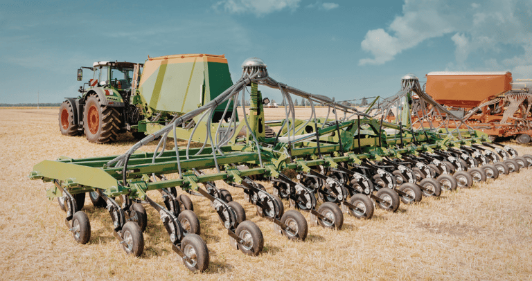 A modern green agricultural tractor pulling a large precision seed drill planter across a harvested field.