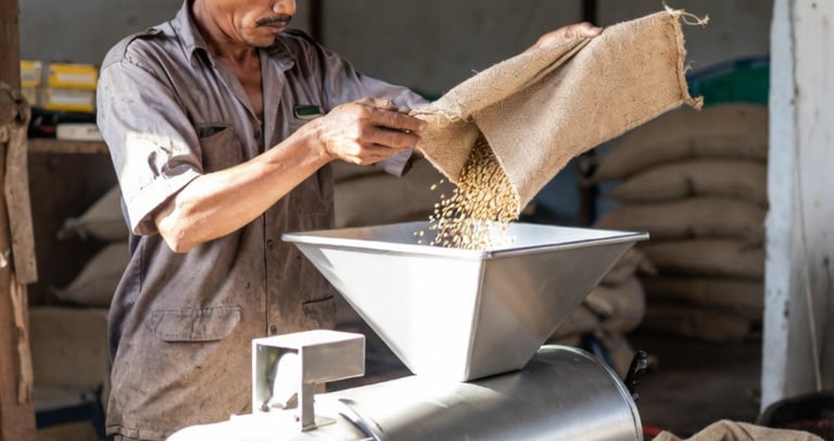 A worker pouring seeds from a burlap sack into a seed traters and coating machine.